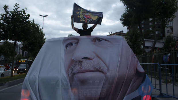 A man holds a flag while travelling in a vehicle adorned with the image of Recep Tayyip Erdogan.