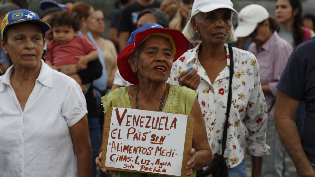 A woman holds a sign that reads in Spanish: “Venezuela, a country without food, medicine, light, and water. Only people.” 
