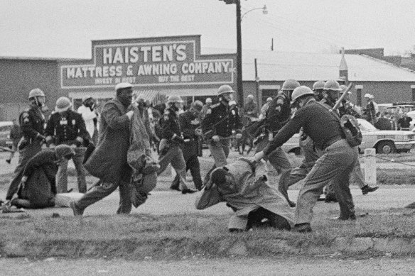 A state trooper swings a billy club at John Lewis, right foreground, chairman of the Student Nonviolent Coordinating Committee, to break up a civil rights voting march in Selma, Alabama, in 1965.