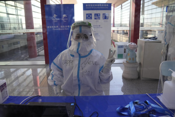 Cheery and covered-up for COVID, a worker poses with “Happy New Year” written on her protective suit at the airport ahead of the 2022 Winter Olympics in Beijing. 
