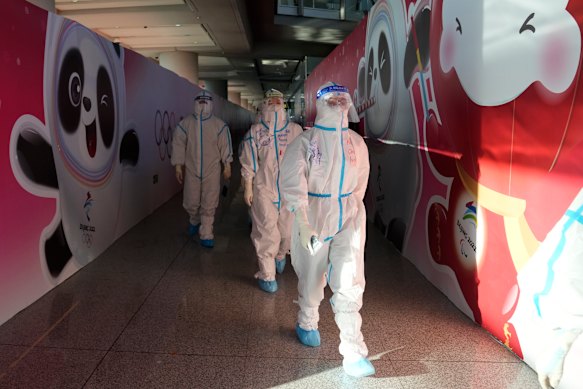 Workers wearing protective gear walk through the airport ahead of the 2022 Winter Olympics.