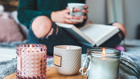 Cropped shot of an unrecognizable young woman relaxing with a book and a cup of coffee on her bed at home A woman relaxing on her bed reading with candles. Photo: iStock