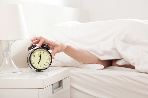 Hand under blanket reaching out for alarm clock