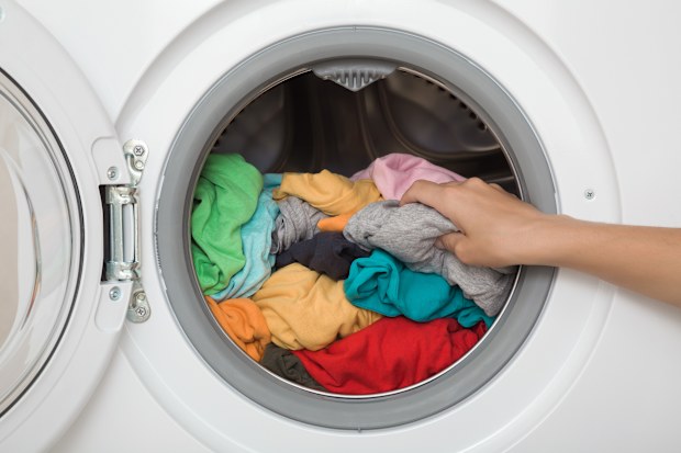 Woman unloading colorful t-shirts from opened white washing machine.