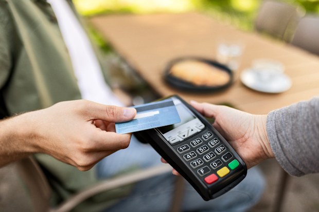 Young man pays to waitress for meal and coffee with credit card in a cafe
