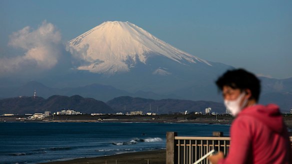 A man wearing a mask visits a beach as snow-capped Mount Fuji is visible in the distance in Fujisawa, Japan.