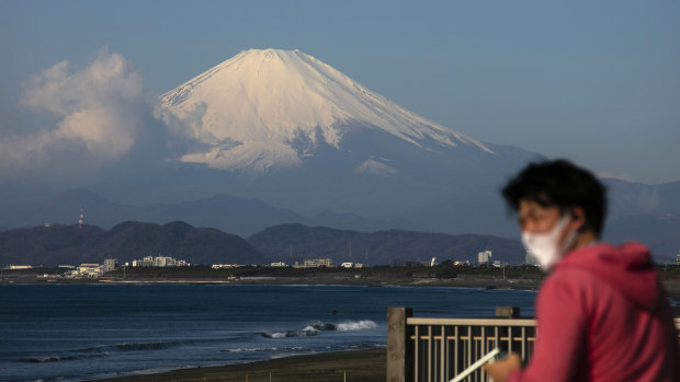 A man wearing a mask visits a beach as snow-capped Mount Fuji is visible in the distance in Fujisawa, Japan.