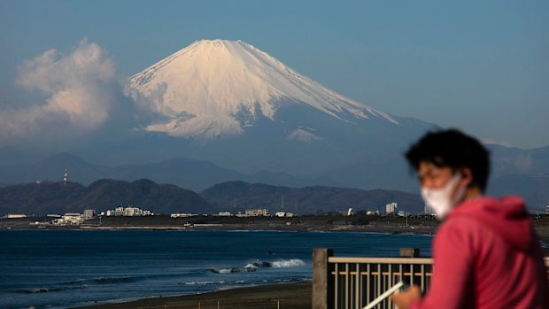 A man wearing a mask visits a beach as snow-capped Mount Fuji is visible in the distance in Fujisawa, Japan.