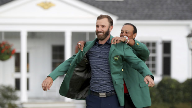 Dustin Johnson is presented the green jacket by Tiger Woods.
