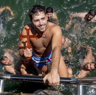 Nicholas Hadzidimitriou, of Mount Waverley, emerges with the cross in the Blessing of the Waters swim off Princes Pier.