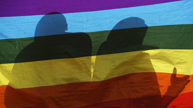 The shadows of people standing behind an LGBT flag.