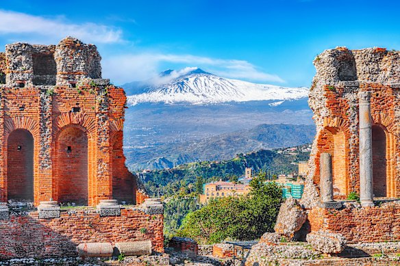 The ruins of an ancient Greek theatre in Taormina, Sicily, frame a snowcapped Mount Etna volcano.