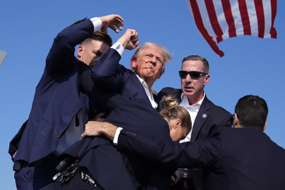 Donald Trump is surrounded by US Secret Service agents with blood on his face.