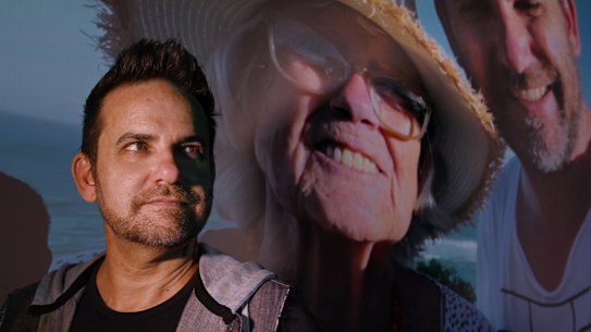 Jason van Genderen stands in front of an image of himself and his mother from the documentary Everybody’s Oma.