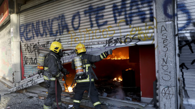 Firefighters force open the bottom floor of a small shopping centre that caught fire amid anti-government protests. The cause of the fire started is unconfirmed.