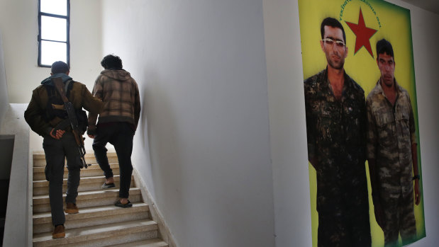 A Kurdish prison security guard, left, escorts a 19-year-old former IS fighter, into the courtroom.