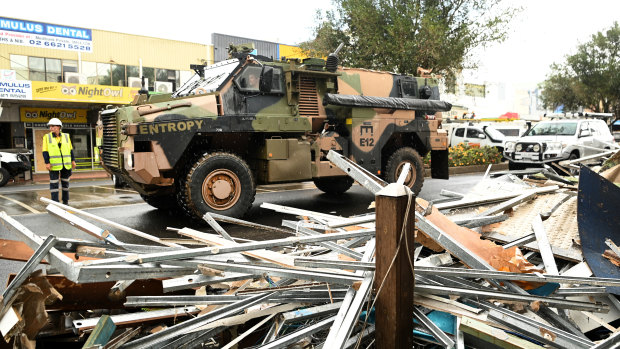 An army vehicle drives past debris in Lismore.