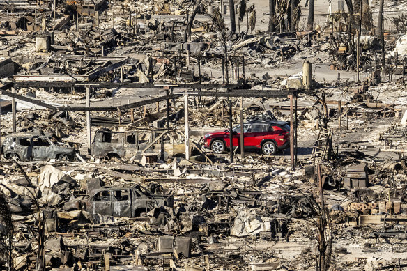 A car drives past homes and vehicles destroyed by the Pacific Palisades fire in Los Angeles.