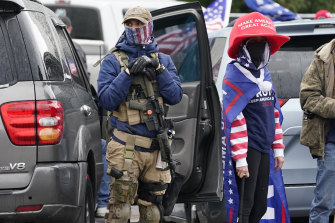 One supporter of President Trump holds a gun as another a baseball bat in front of the Oregon State Capitol building.