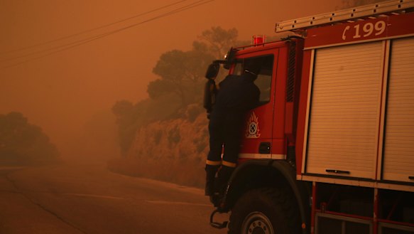 A fire truck is engulfed in a pall of orange smoke on a road near Kineta, west of Athens.