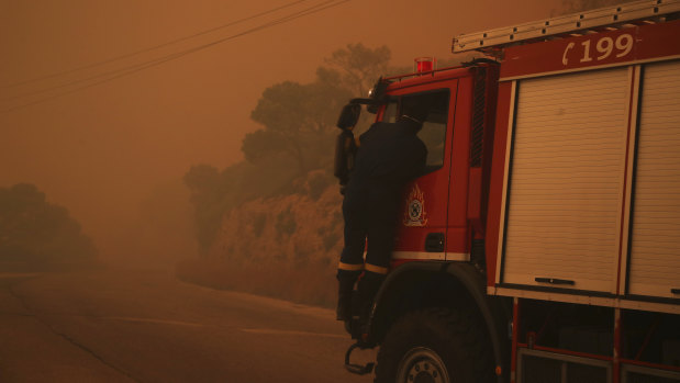 A fire truck is engulfed in a pall of orange smoke on a road near Kineta, west of Athens.