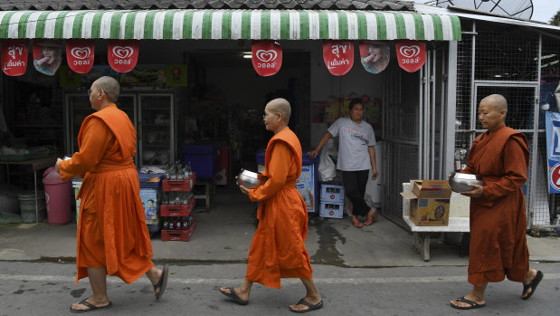A woman watches female monks pass by her shop on their morning alms rounds.