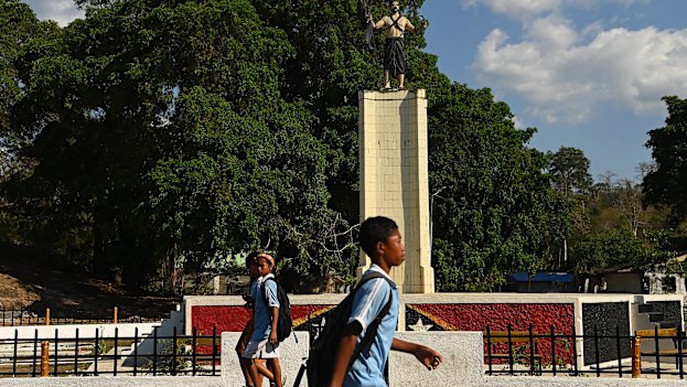 Timorese school students walk past what was the Indonesian unification statue that is now a memorial in Balibo. On gaining independence, the original red and white flag of the statue was painted black. 