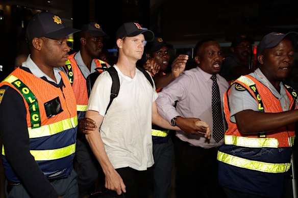 Steve Smith was escorted by police officers to a departure area at OR Tambo International airport in Johannesburg.