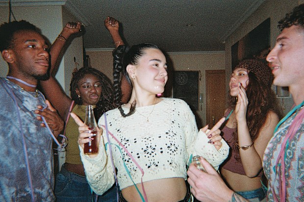 Young adults enjoying a house party, laughing and dancing while holding bottles and wearing streamers for a fun celebration