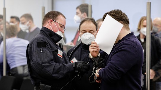 The defendant hides his face as he is led into a courtroom of the Higher Regional Court in Dresden.