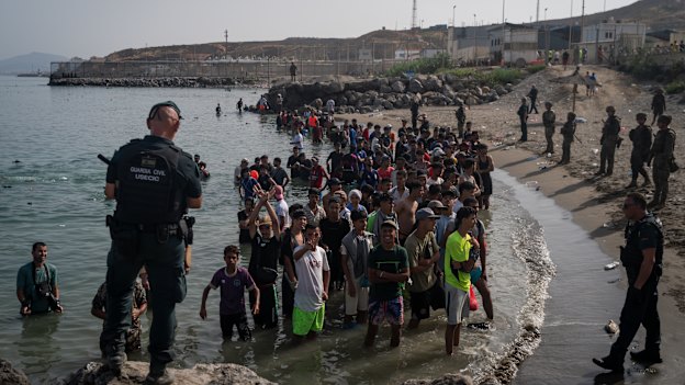 Members of the Guardia Civil USECIC guard migrants on Tarajal beach after crossing the border between Spain and Morocco in Ceuta.