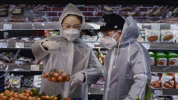 A Chinese couple wears plastic coats and protective masks as they shop for groceries at a supermarket in Beijing on February 11.