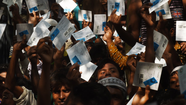 Men and boys hold their ration cards in the air  at a Red Cross distribution point in Burma Para refugee camp, at  Cox’s Bazar, Bangladesh.  