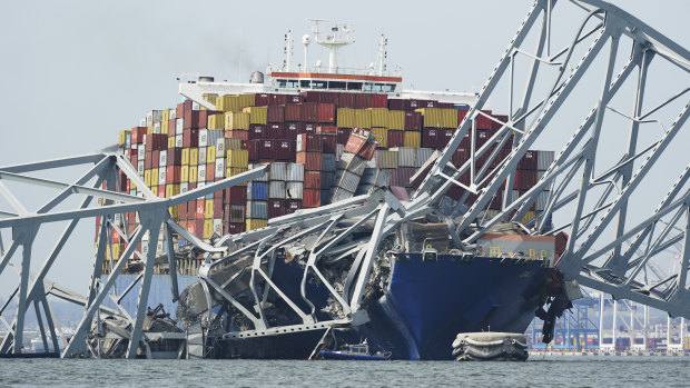 A Coast Guard cutter passes a cargo ship that is stuck under part of the destroyed Francis Scott Key Bridge.