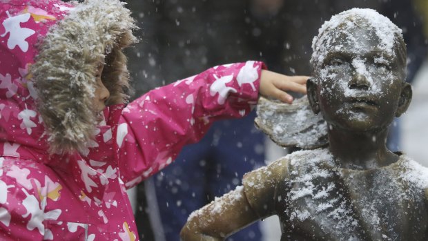 A young girl brushes off snow on the Fearless Girl statue in lower Manhattan.
