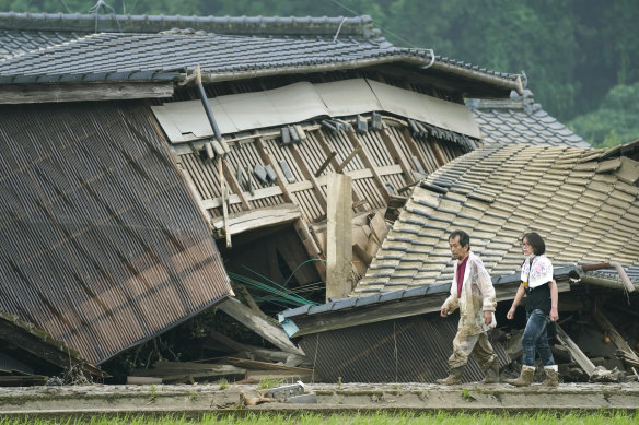A couple walks in front of houses damaged by flood in Kuma village, Kumamoto prefecture, south-western Japan, on Sunday.