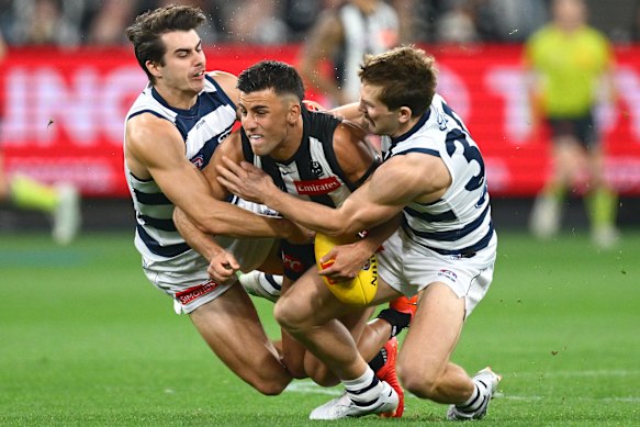 Nick Daicos of the Magpies is tackled by Oisin Mullin and Tom Atkins of the Cats.