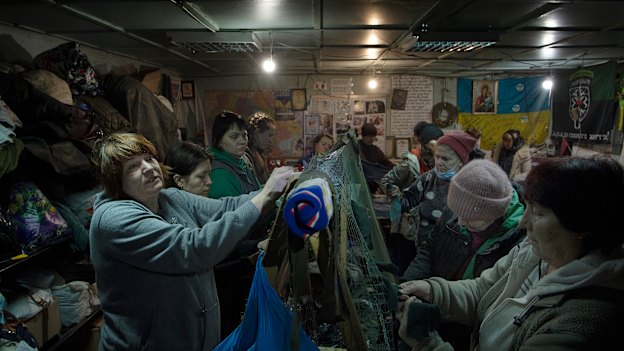 A group of women tie strips of donated material into camouflage nets in a shelter in Uman.