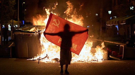 Un manifestante tiene una bandiera accanto ai bidoni della spazzatura in fiamme durante gli scontri con la polizia a seguito di una manifestazione sulla crisi immobiliare in Spagna.