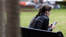 A woman uses her phone while sitting on a park bench