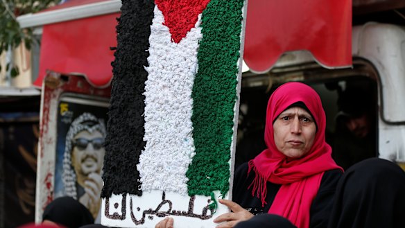 A Palestinian woman holds a symbolic of the Palestine flag with Arabic words that read: "Palestine for us" at a refugee camp, south of Beirut.