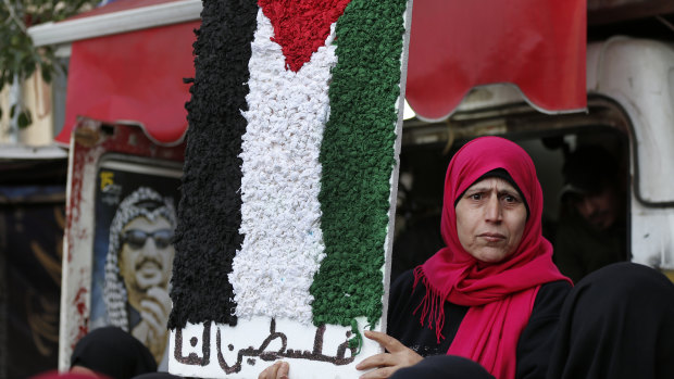A Palestinian woman holds a symbolic of the Palestine flag with Arabic words that read: "Palestine for us" at a refugee camp, south of Beirut.