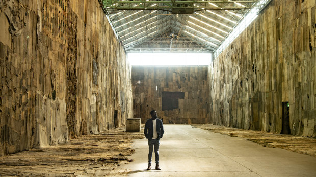 Ibrahim Mahama stands inside Cockatoo Island's Turbine Hall surrounded by his vast art installation No Friend but the Mountains