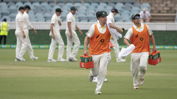 Substitute fielders Tom Vane-Tempest and Dan Leerdam run drinks out to the Australian cricket team.