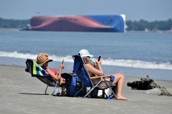 Beachgoers relax on Jekyll Island's Driftwood Beach as the Golden Ray cargo ship is capsized in the background.