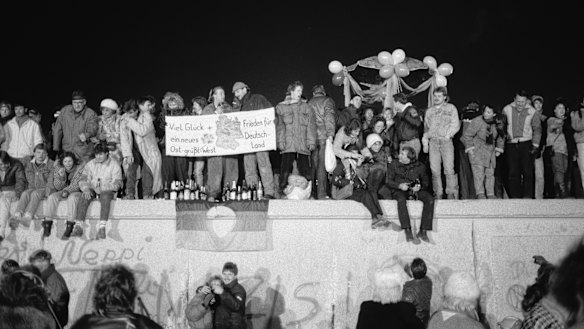 Revellers gather on the Berlin Wall to celebrate the New Year and the effective end of the city's partition, on December 31, 1989. A banner reads ''Good luck and peace for a new Germany - East Greets West''.