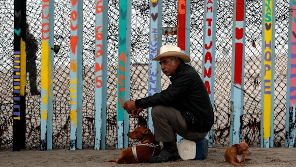 A local resident sits with his dogs in front of the US border fence at the beach in Tijuana, Mexico.
