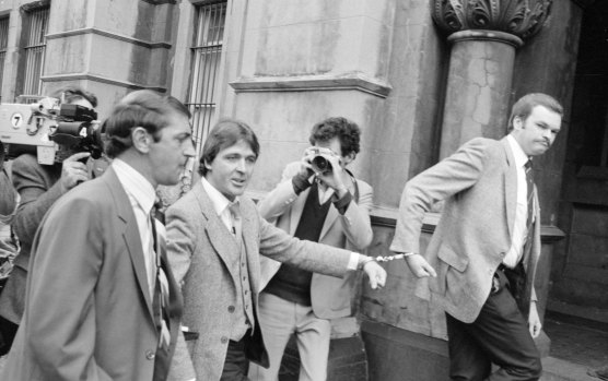 Christopher Dale Flannery (second from left) is led handcuffed into Melbourne’s City Watch House in October 1981 to be charged with the murder of Roger Wilson.