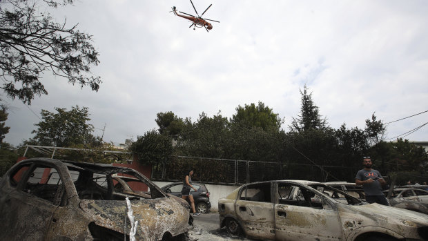 A firefighting helicopter flies above burnt-out cars in Mati, east of Athens.