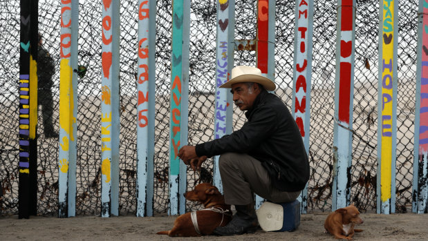 A local resident sits with his dogs in front of the US border fence at the beach in Tijuana, Mexico.